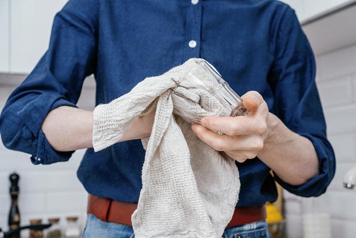 Homme essuyant un verre avec un torchon de cuisine. source : spm