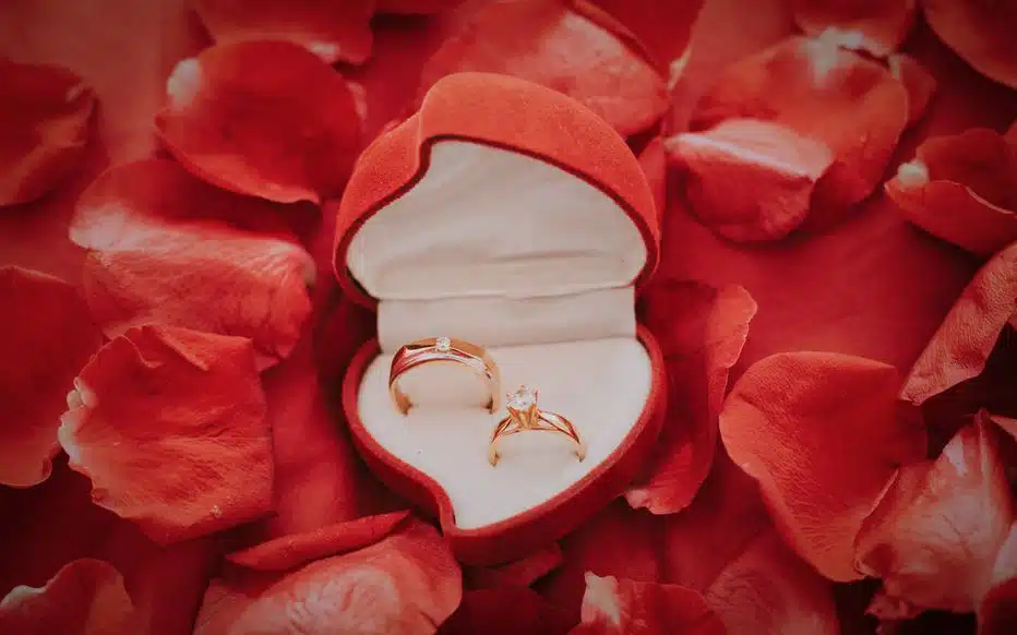 Un homme élégant est à genoux, tenant un écrin à bijoux, devant une femme émue aux larmes.