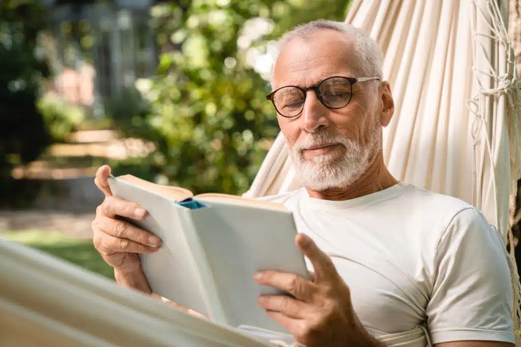Homme âgé détendu dans un hamac, lisant un livre