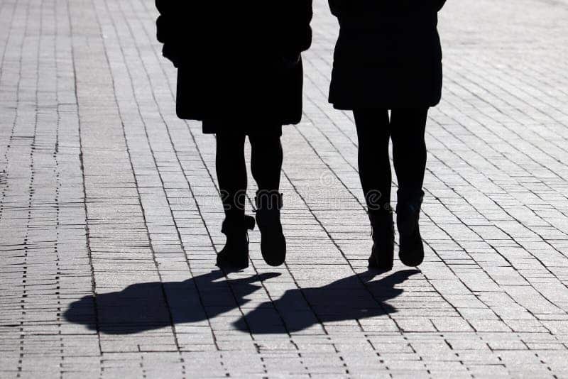 Deux femmes marchant côte à côte dans une rue pavée, symbolisant une relation naissante